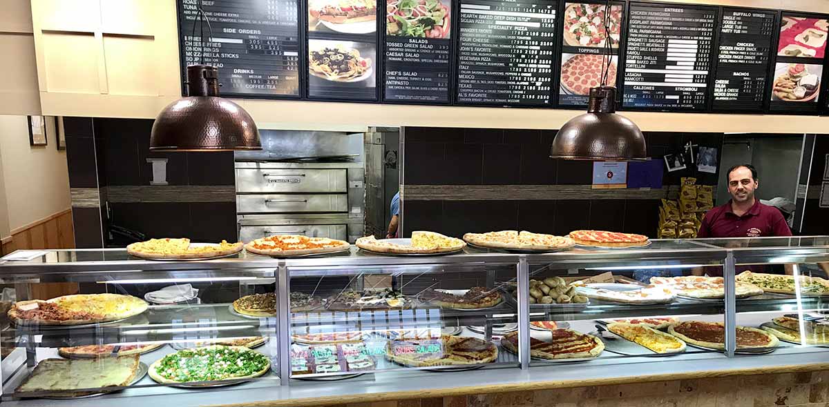 Photo of display shelves with 20 kinds of pizzas, with an overhead menu board
